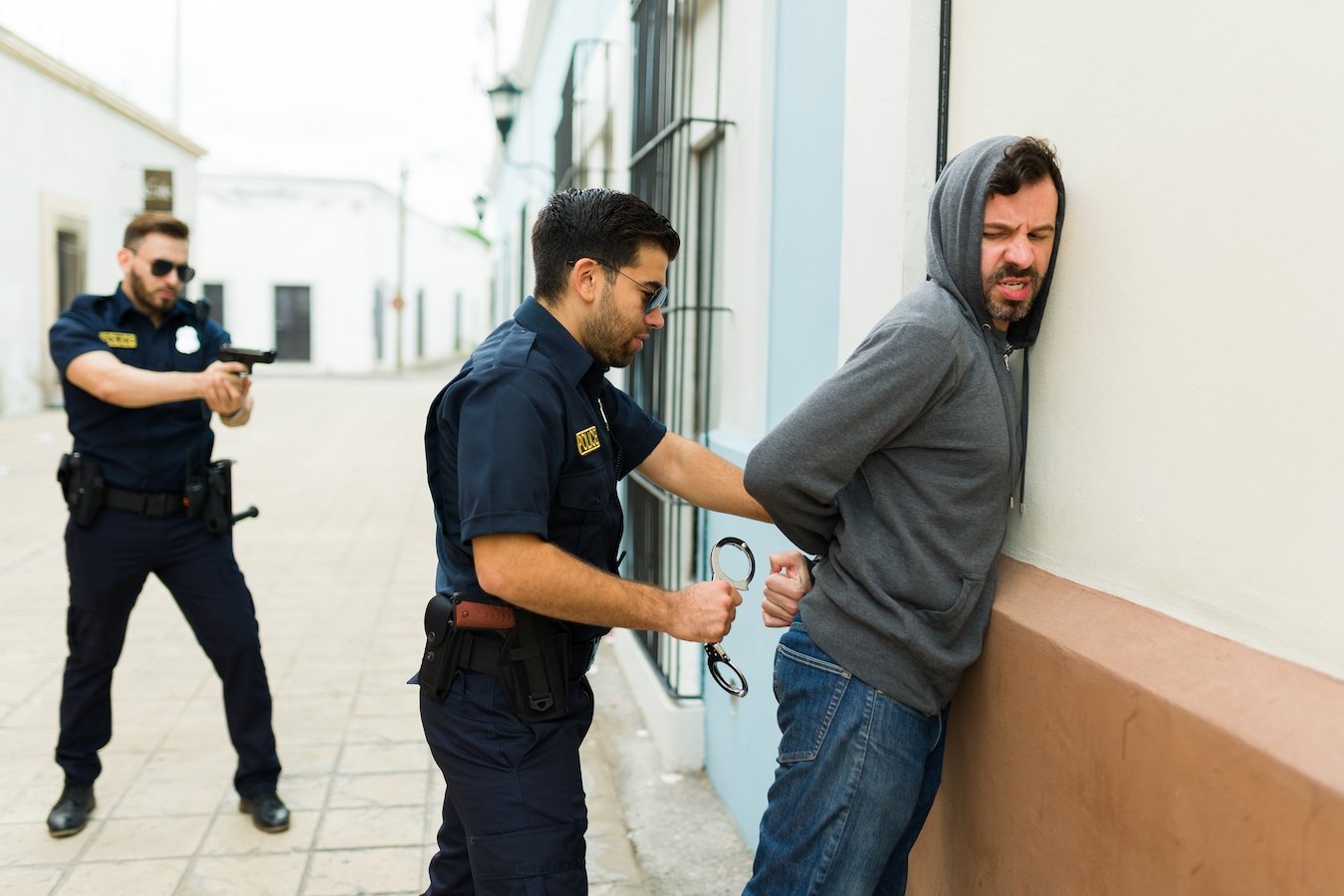 Hombre con capucha siendo arrestado y esposado mientras es presionado contra la pared.