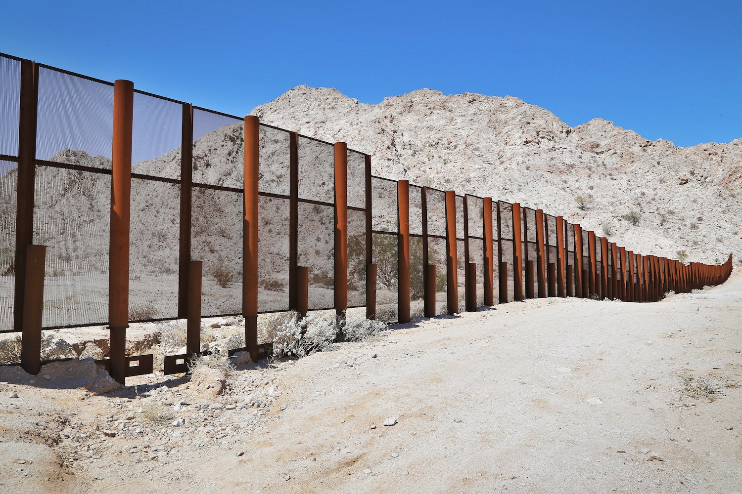Daylight view of the border wall between the U.S. and Mexico, with mountainous terrain in the background