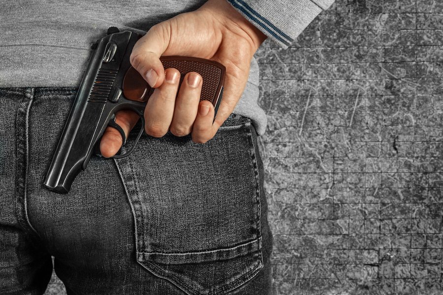 Closeup of man holding a gun behind his jeans pockets in an apparent attempt to hide it