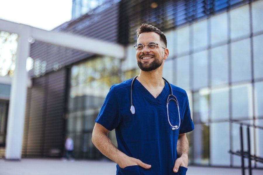 Smiling male nurse in scrubs outside of a medical facility