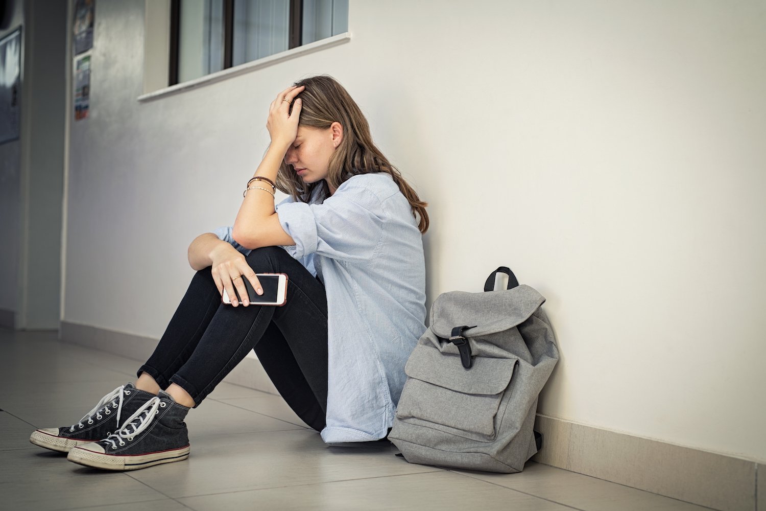 Adolescente sentada contra una pared con su mochila mirando angustiada después de ser descubierta por ausentismo escolar Adolescente sentada contra una pared con su mochila mirando angustiada después de ser descubierta por ausentismo escolar