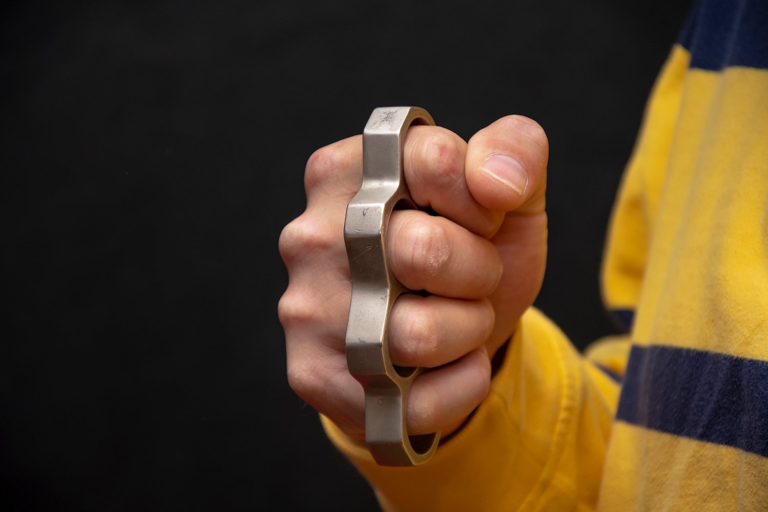 Closeup of man's clenched fist with metal knuckles against a black background
