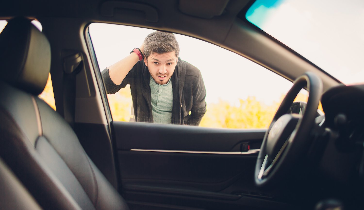 Man looking into a car driver's side window that is parked