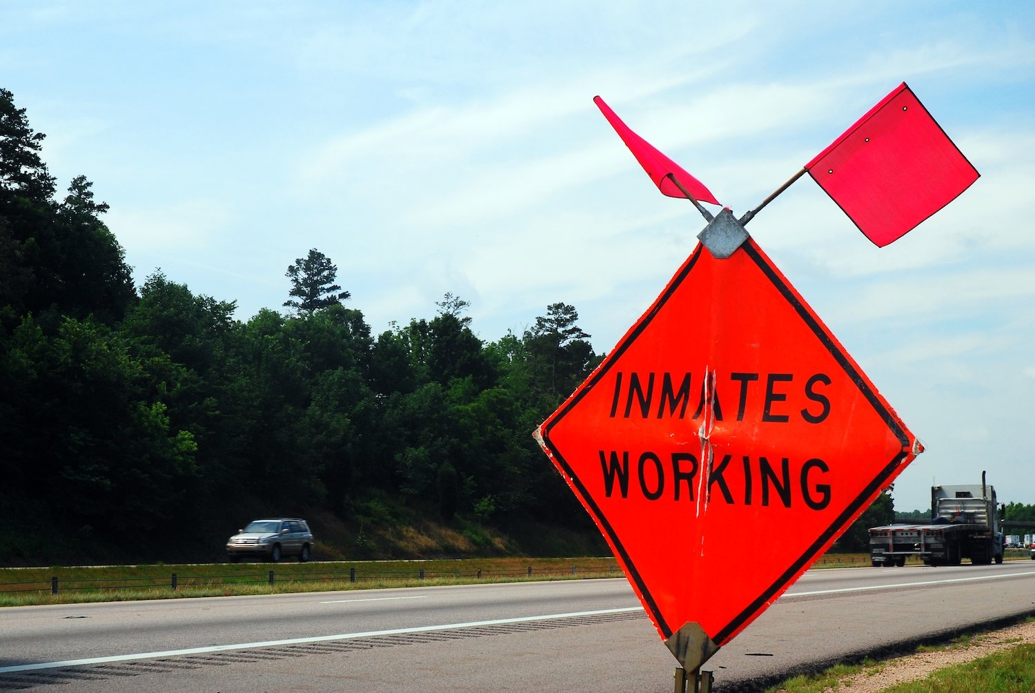 Street sign that says "Inmates Working" by a highway
