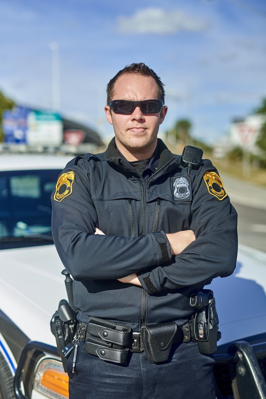 Oficial de policía bajo el 830.1 PC posando frente a su auto de policía durante el día