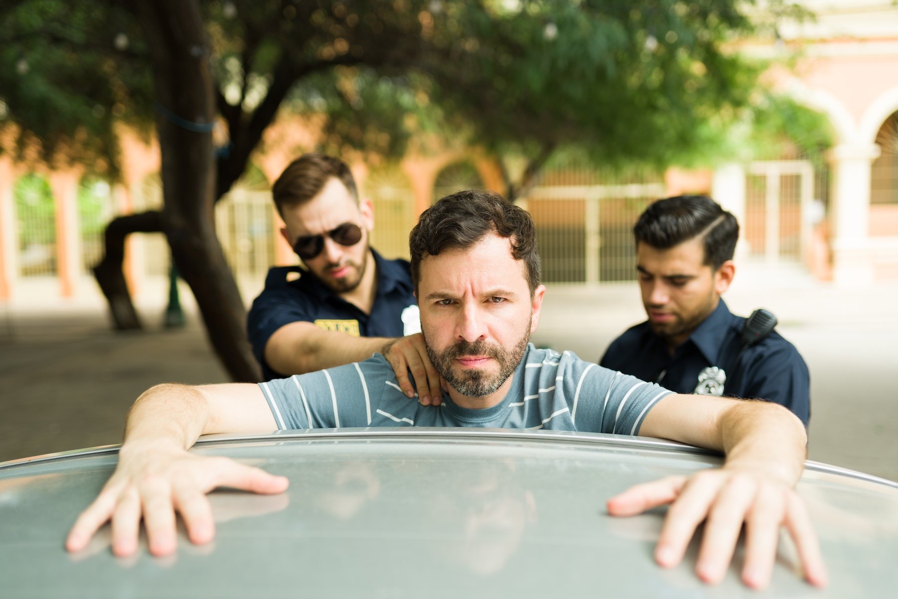 Dos oficiales de policía arrestando a un hombre que está apoyado contra su auto