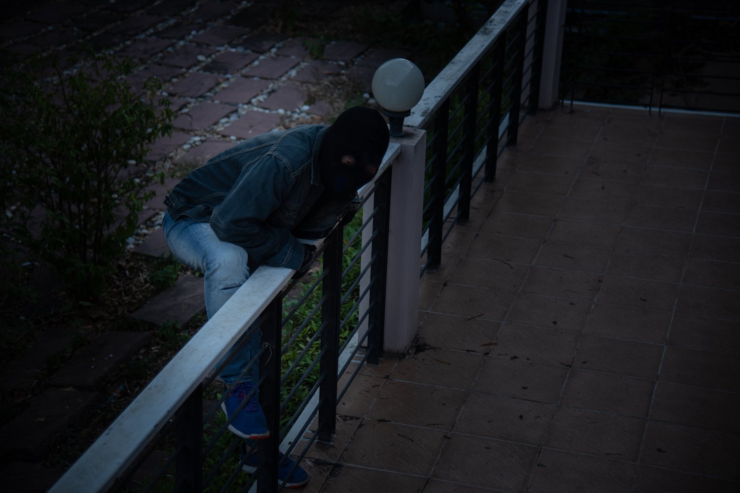 Ladrón encapuchado escalando una cerca de patio para entrar a la casa y robar