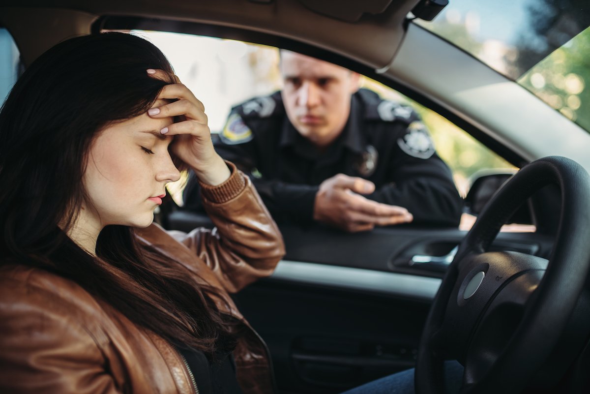 Woman driver holding her head in her hand while a police officer during a traffic stop studies her driver's license
