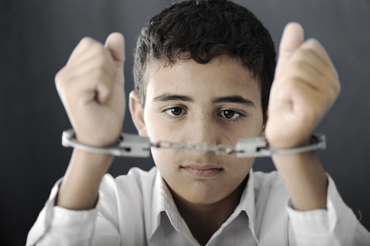 Niño levantando las manos esposado contra un fondo gris