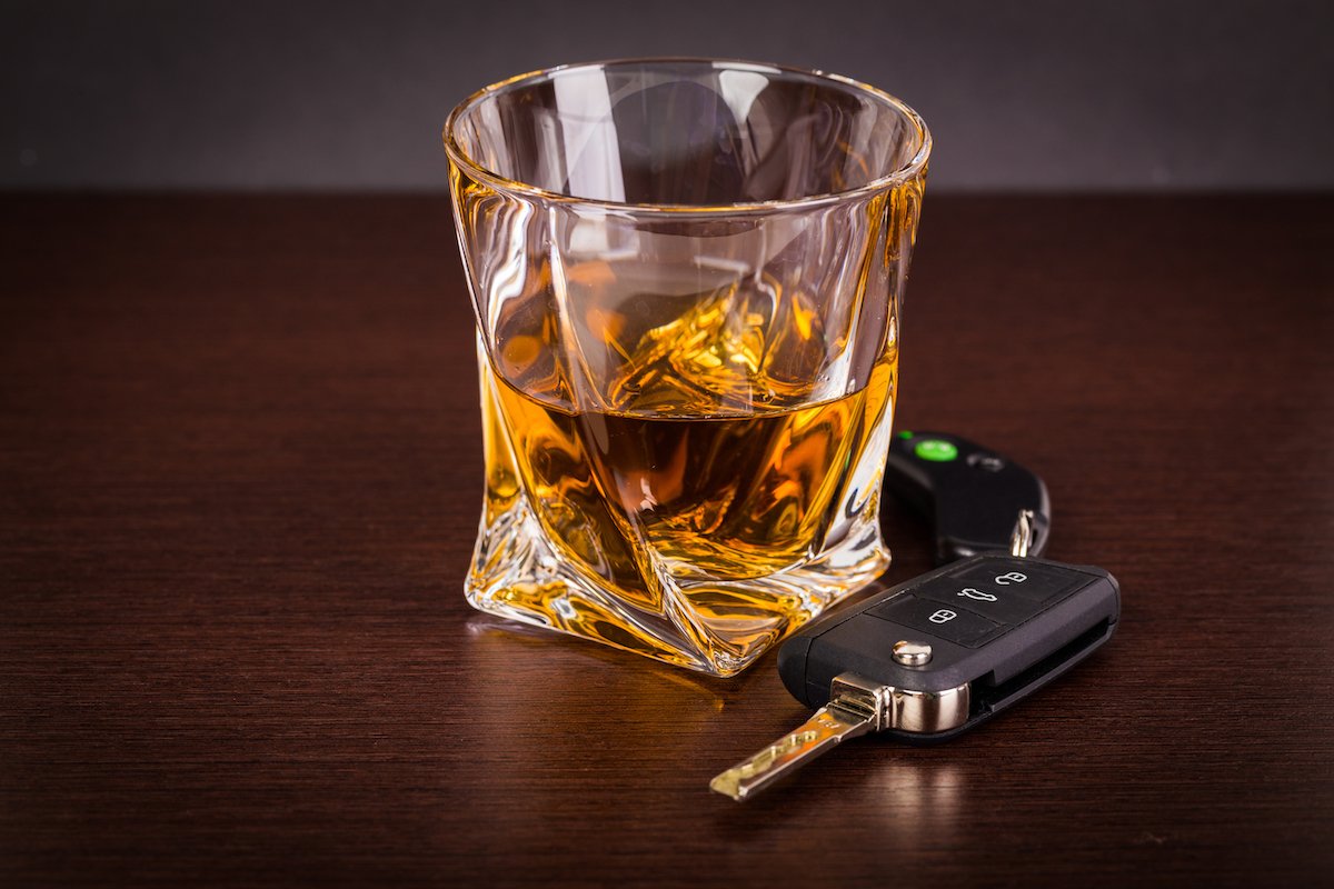 Tumbler of alcohol and a car key on a wooden table