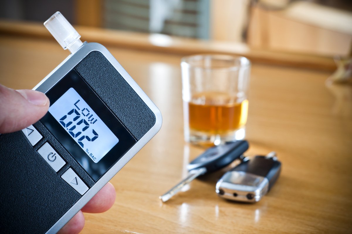 Breathalyzer showing a 0.02% BAC near a table showing a tumbler of alcohol and car keys
