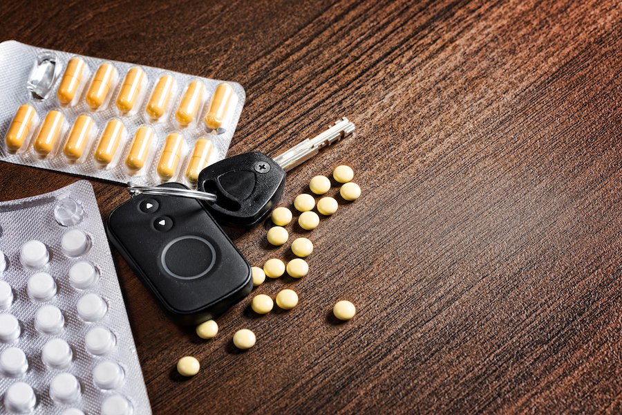 Packets of tablets and capsules next to car keys on a wooden table