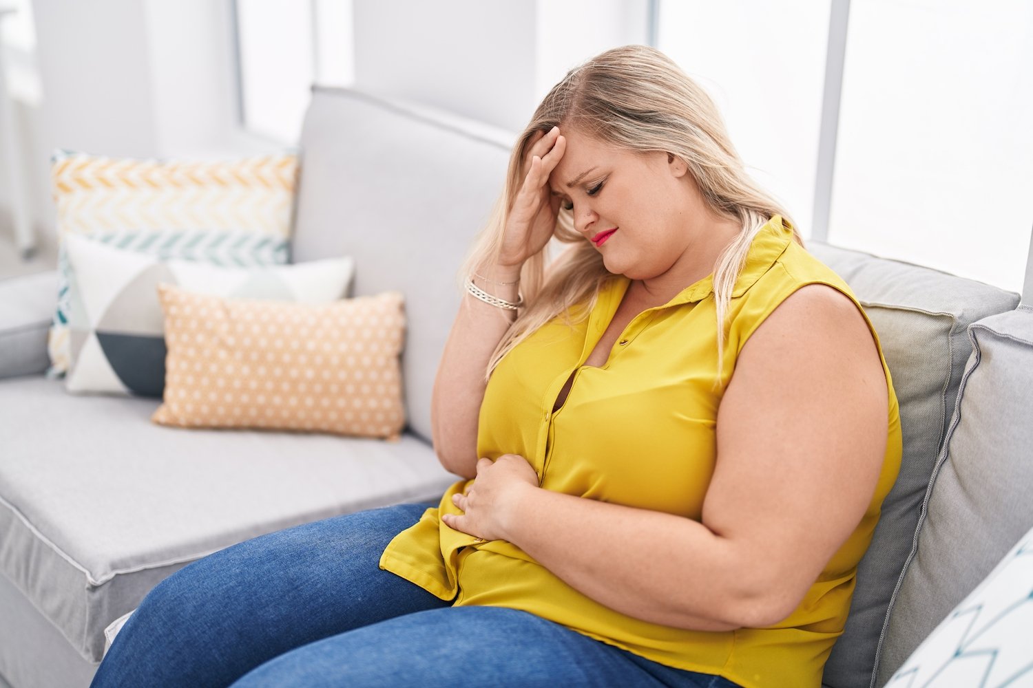 Overweight woman on a couch clutching her stomach in pain
