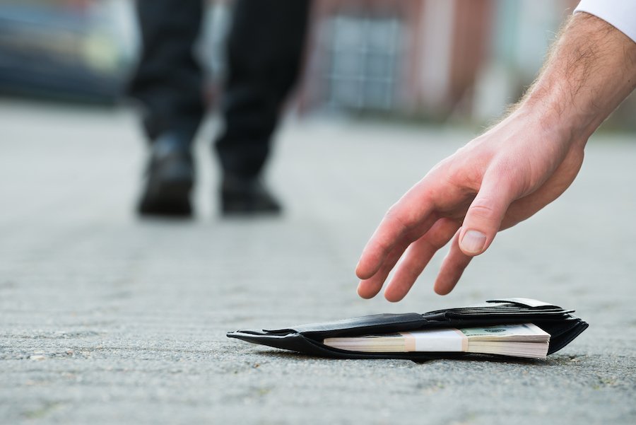 Cropped hand of businessman picking up fallen wallet with money on street in violation of NRS 205.0832(d)