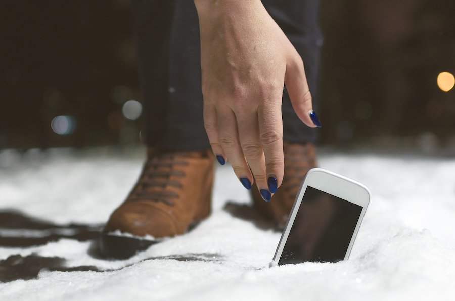 Hand reaching down to pick up a lost cell phone on the snowy ground