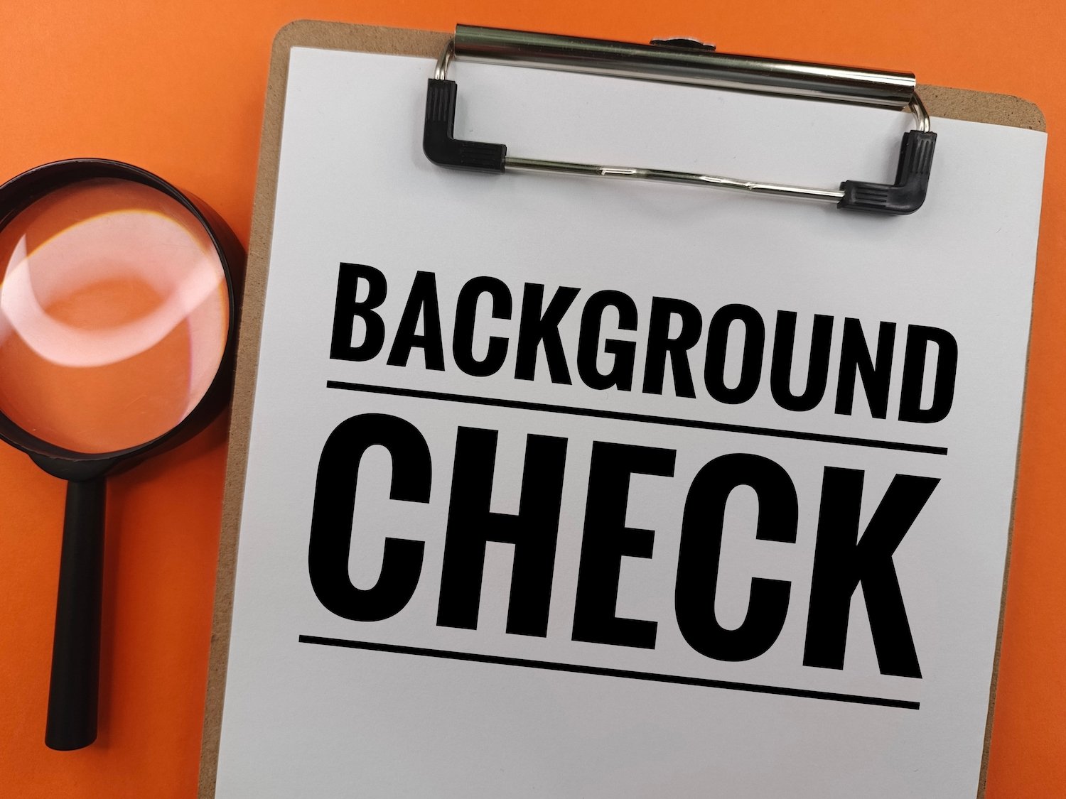 Portapapeles sosteniendo un papel que dice, “Chequeo de antecedentes” junto a una lupa