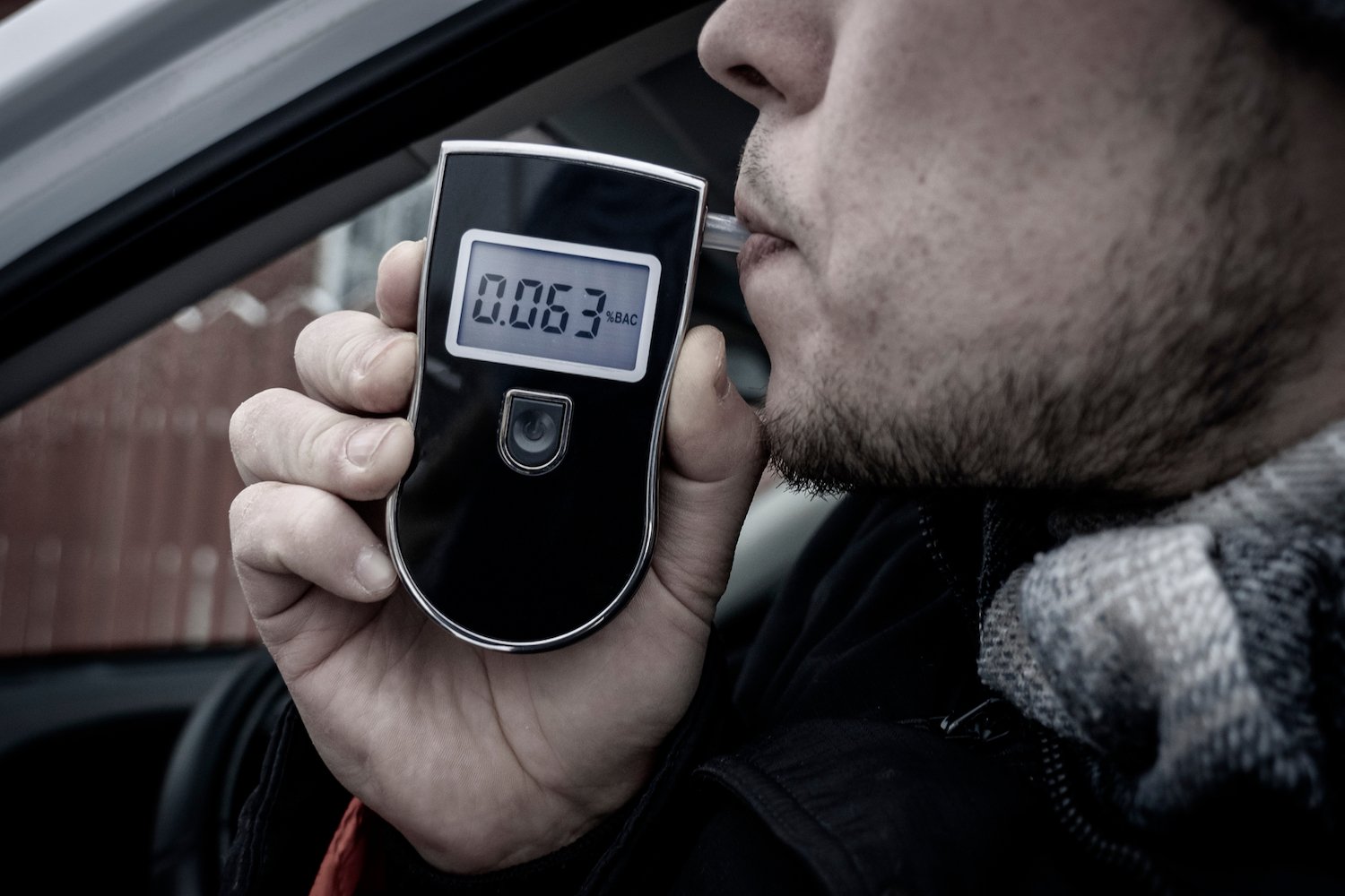 Closeup of driver breathing into a breathalyzer while he is driving on a suspended license