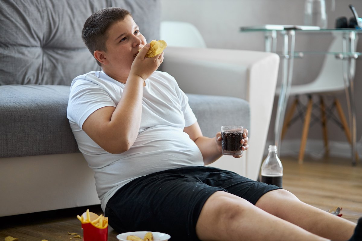 Overweight boy eating fast food on the floor in his living room