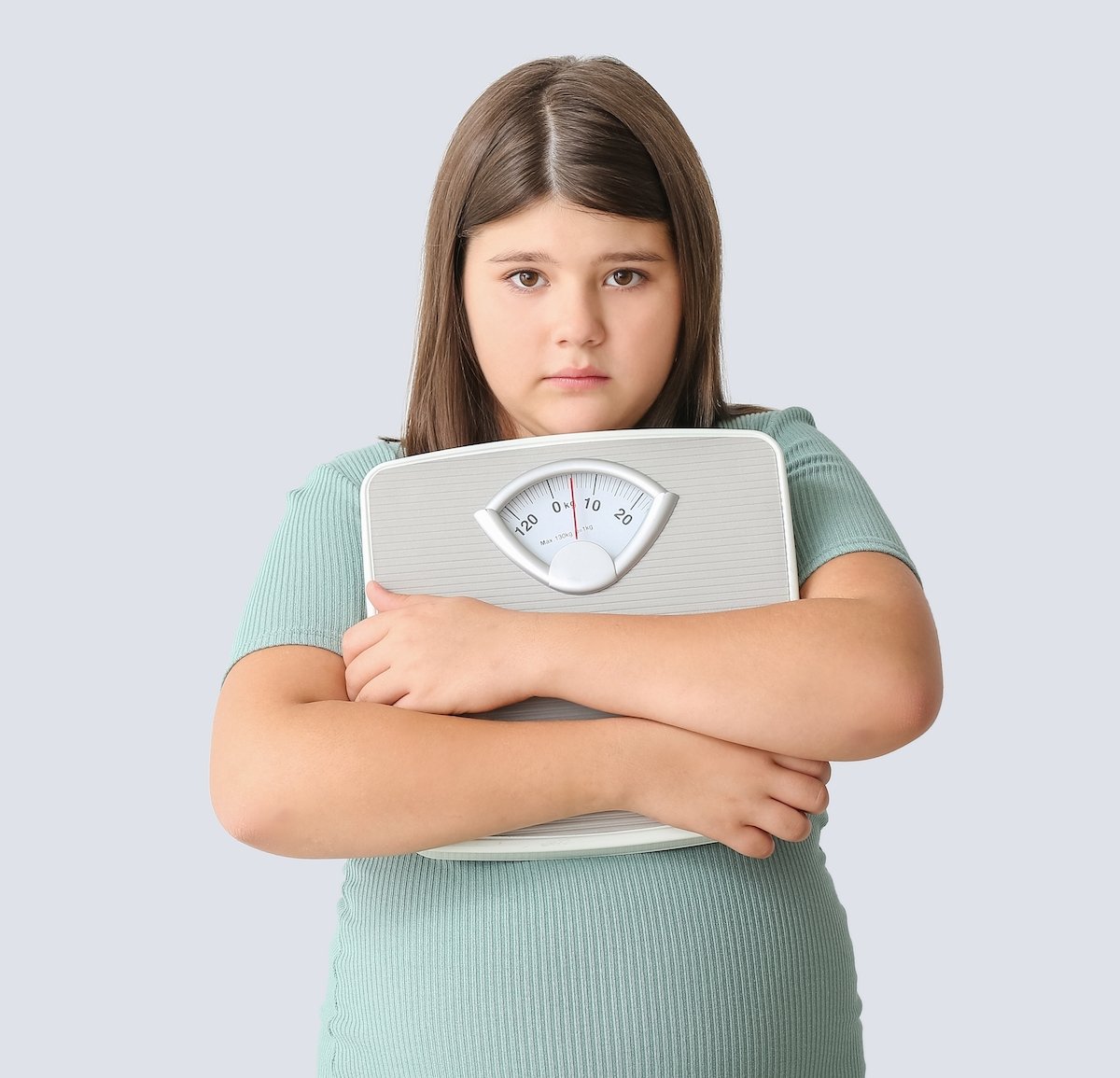 Overweight girl holding a scale against a grey background