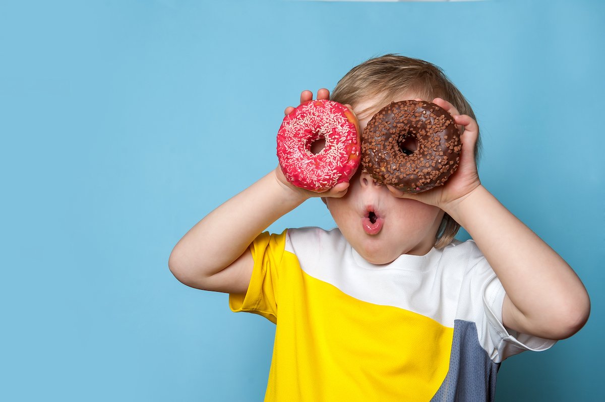 Young boy holding up donuts to his eyes against a blue background