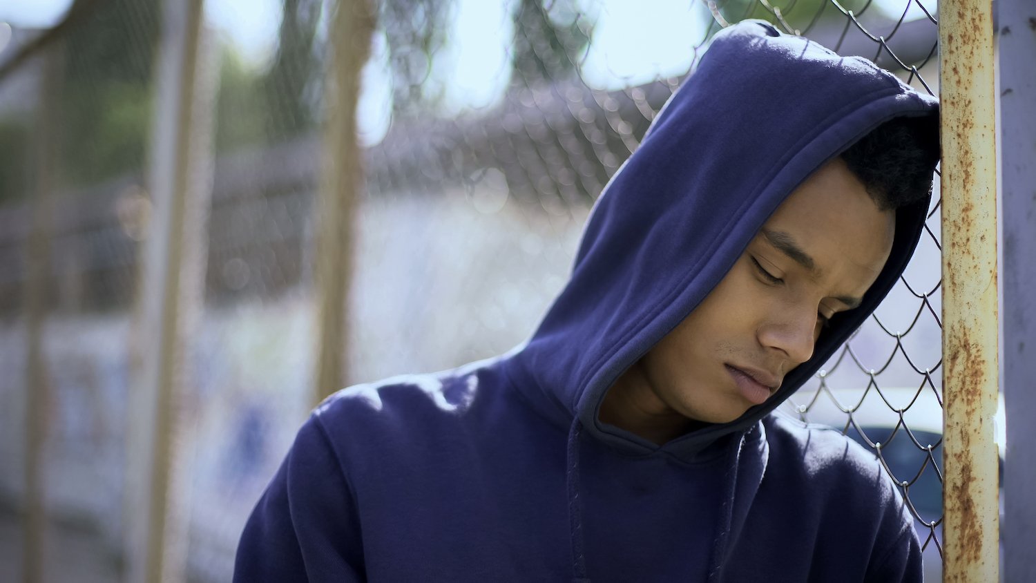Niño con sudadera con capucha apoyado contra la puerta en la detención juvenil