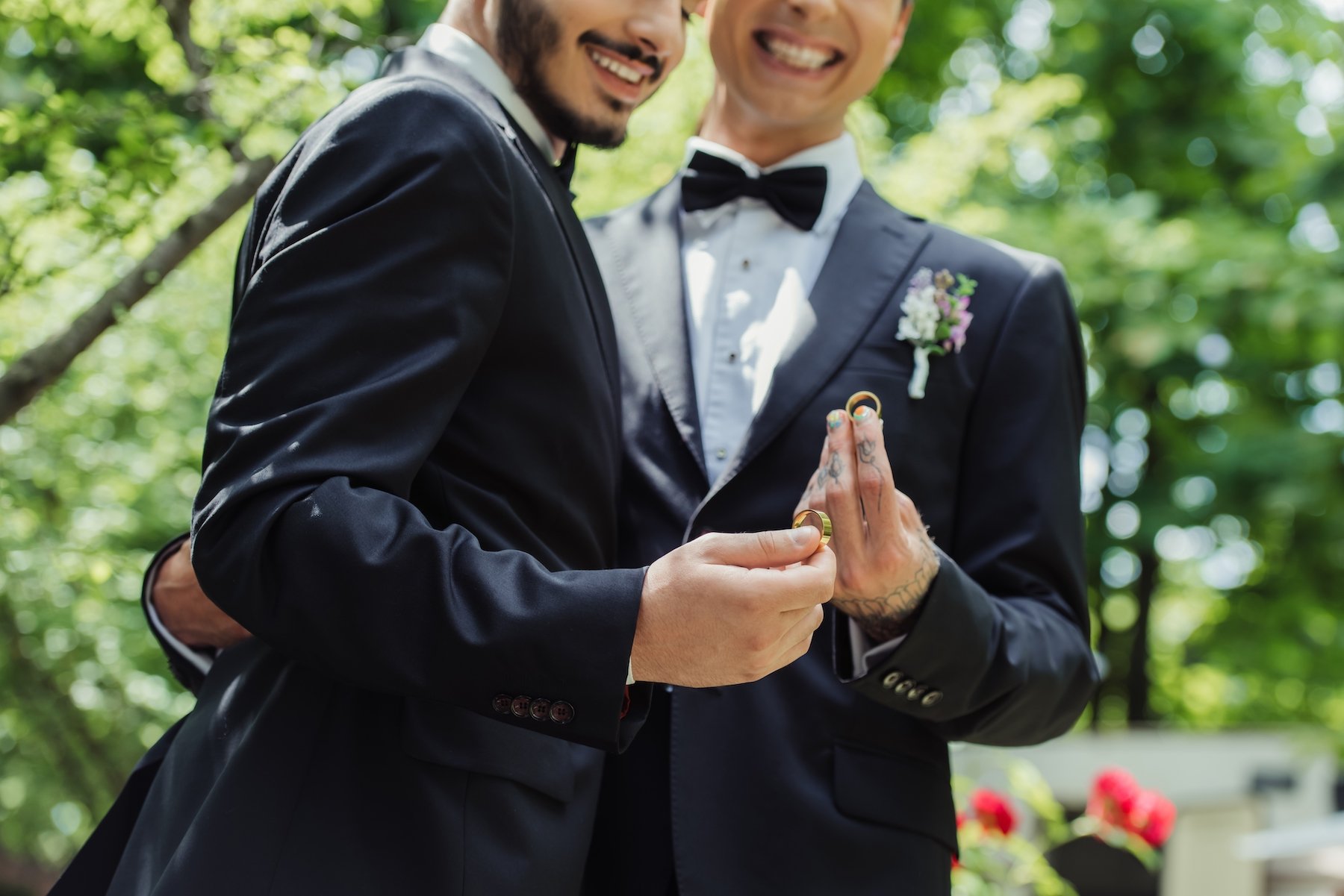 A gay couple in tuxedo on their wedding day holding up rings