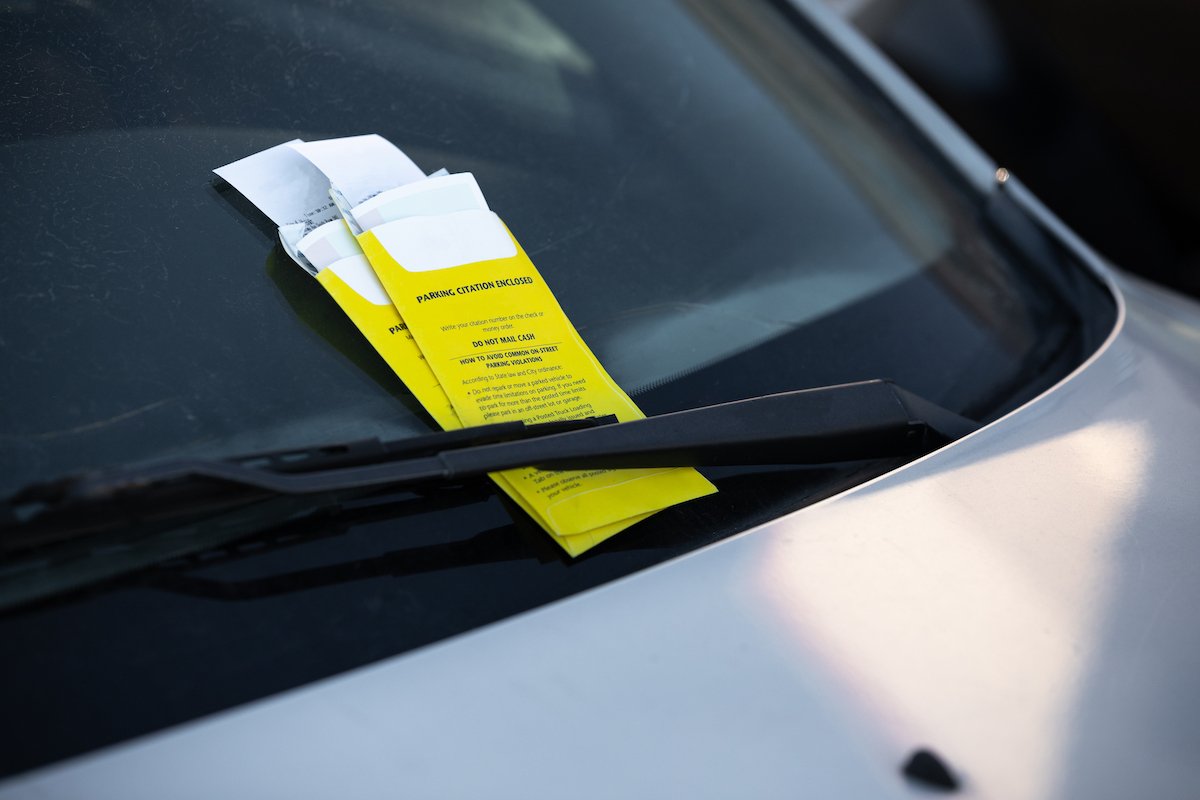 Closeup of a car windshield with two tickets tucked underneath the windshield wiper