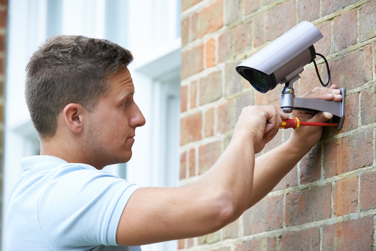 Man installing a security camera outside of his brick home