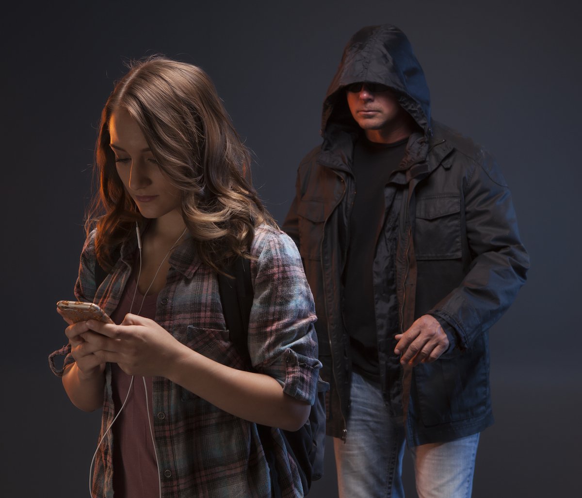 Man in hoodie approaching a teenager on her phone in a dark alley