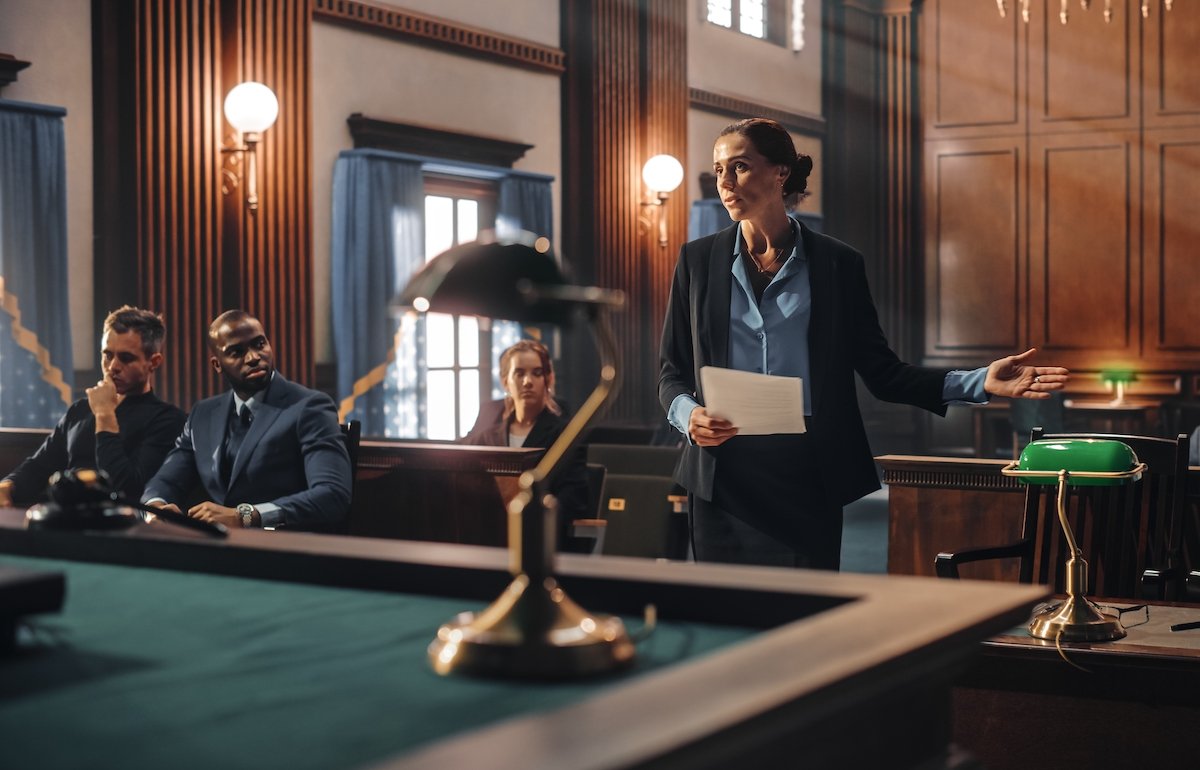 District attorney speaking in court while the defense attorney and his client look on