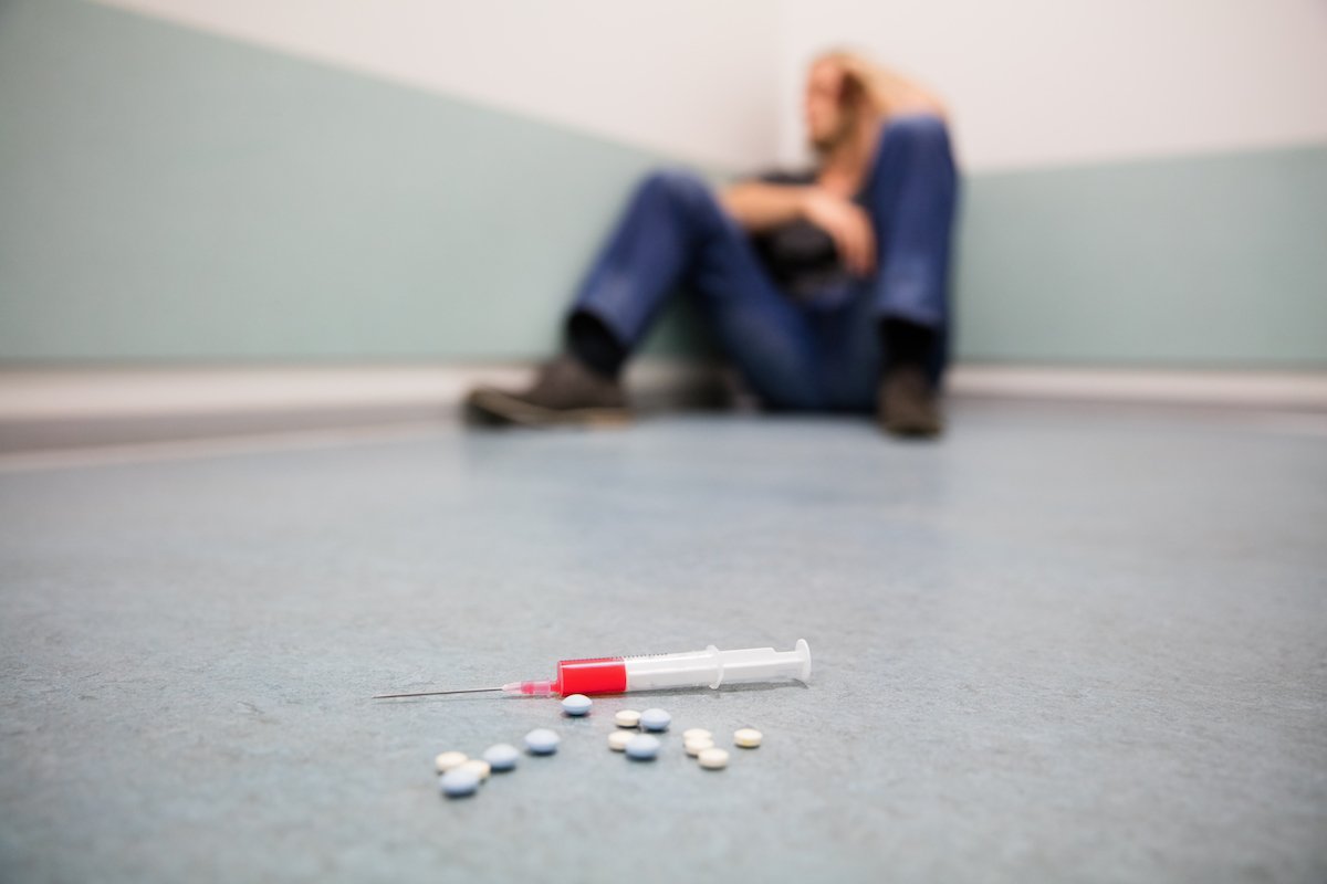 Heroin user cowering in the corner with a drug and pills in the foreground