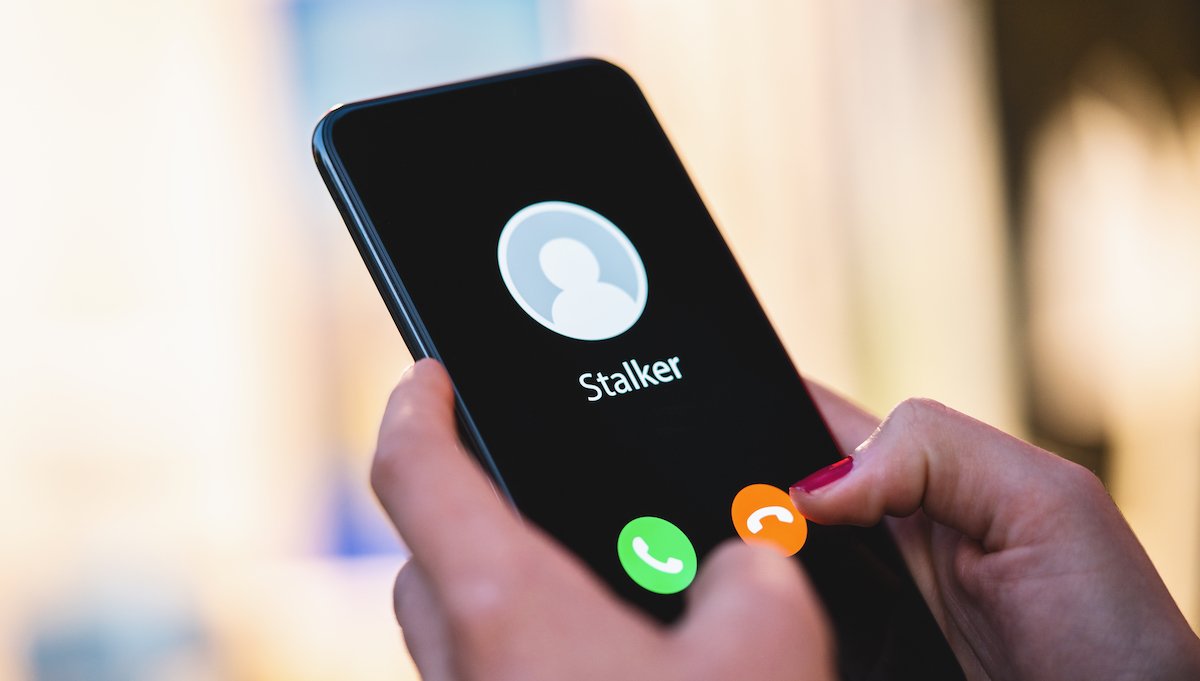 Mujer sosteniendo un teléfono con una llamada entrante de un contacto llamado “Acosador”