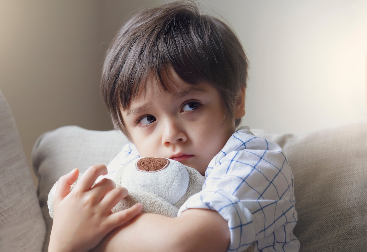 Young boy clutching a teddy bear in a room after a CRS 18-6-601 violation