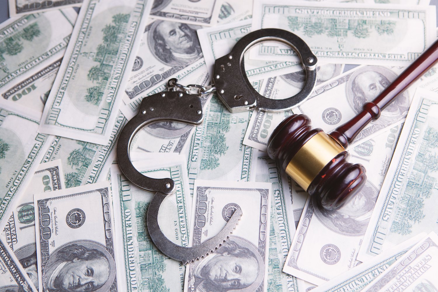 Open handcuffs and a judge's gavel on a table covered with cash