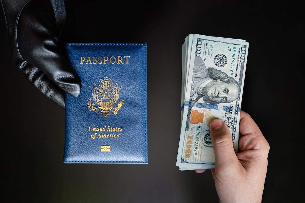 Gloved hand holding a passport next to a bare hand holding several hundreds of dollars in cash.