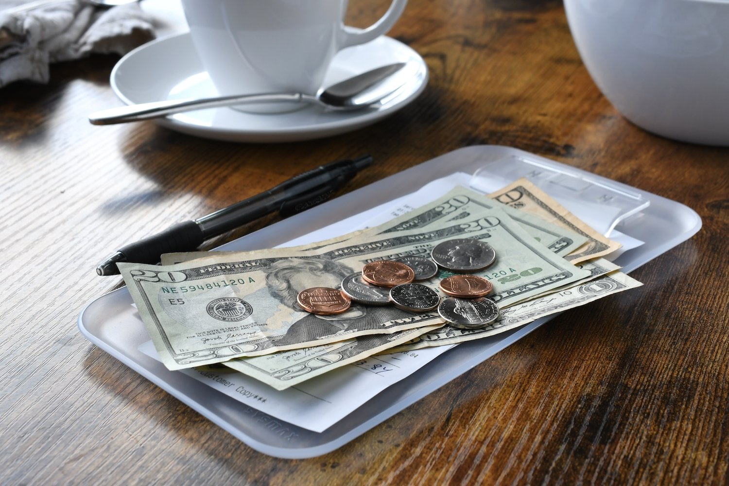 Dinero en efectivo y monedas dejados como propina en una mesa de restaurante junto a una taza de café