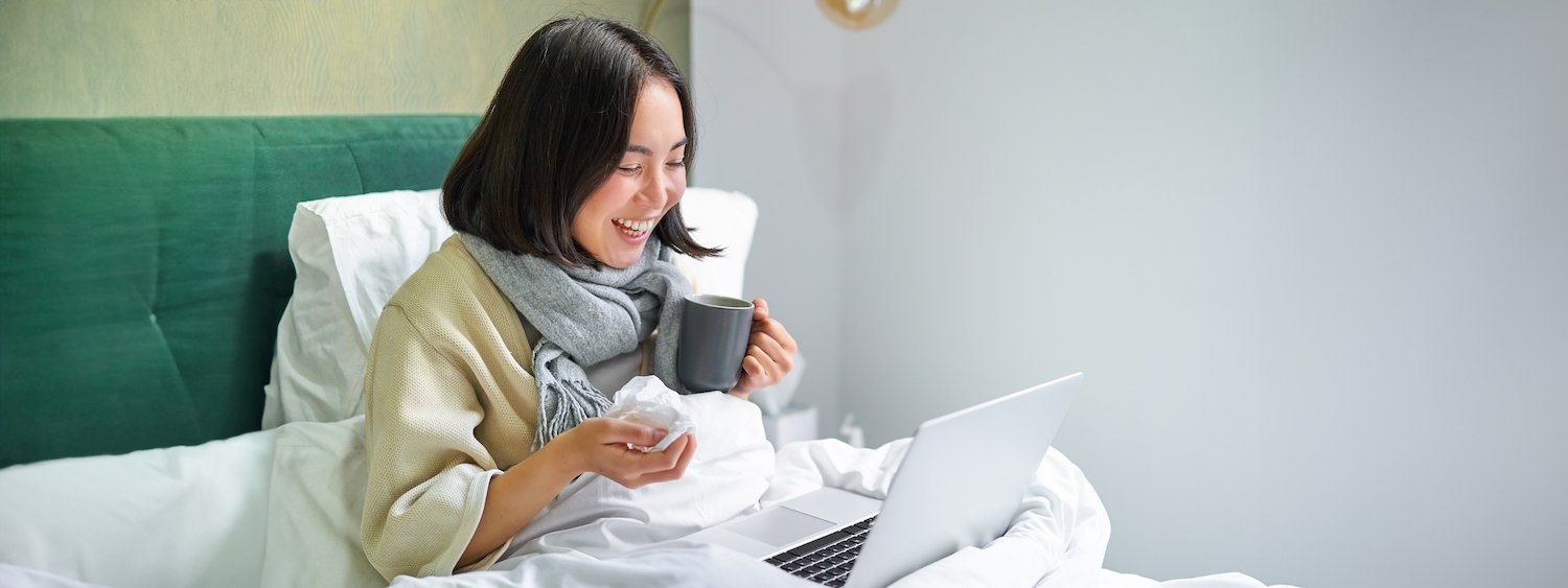 Employee home from work sick in her bed looking at her laptop