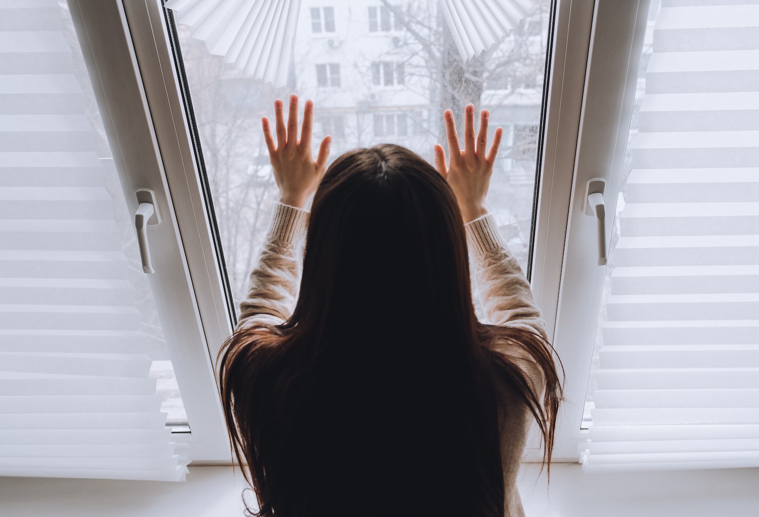 Mujer en arresto domiciliario sosteniendo el marco de la ventana y mirando hacia afuera