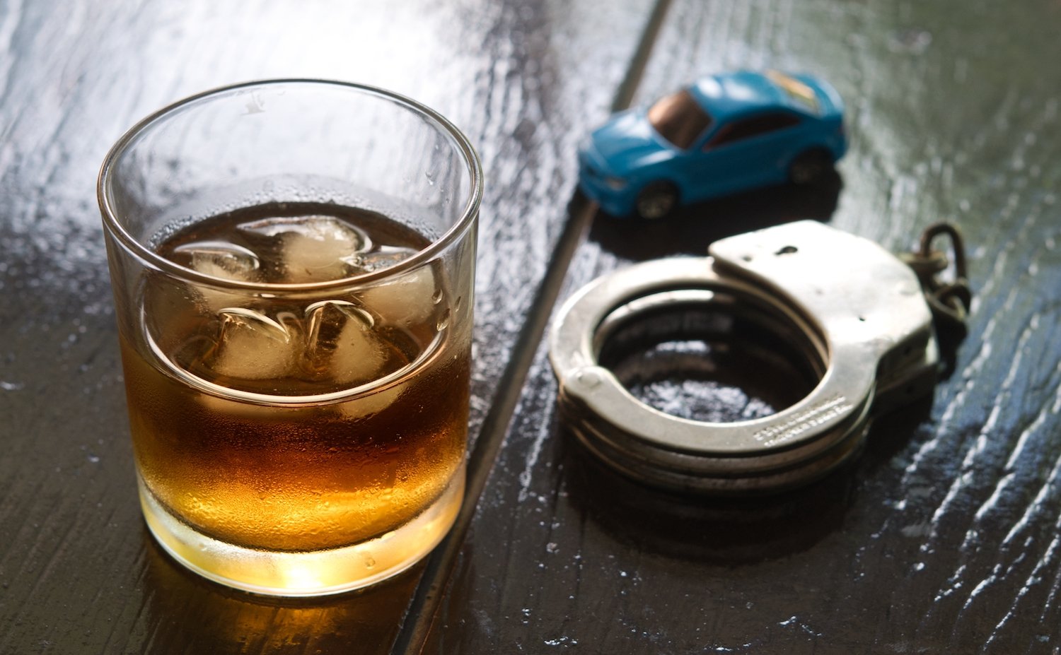 Tumbler of alcohol, a toy car, and handcuffs on a wooden table