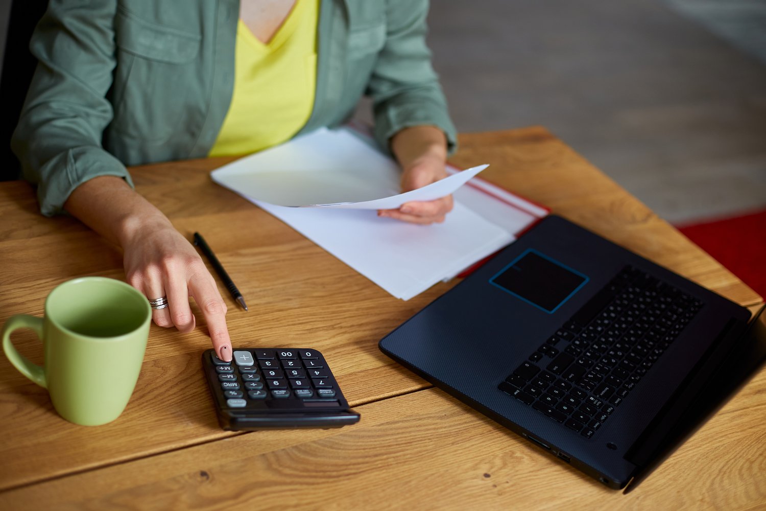 Mujer empleada en su escritorio usando su calculadora y su laptop para calcular su tarifa regular de pago
