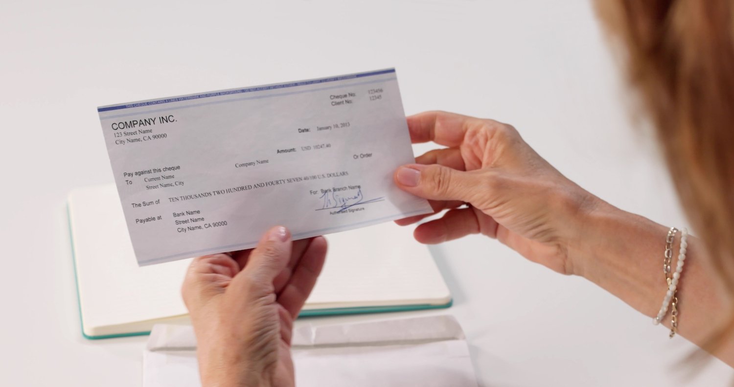 Mujer empleada sosteniendo su cheque de pago en su escritorio