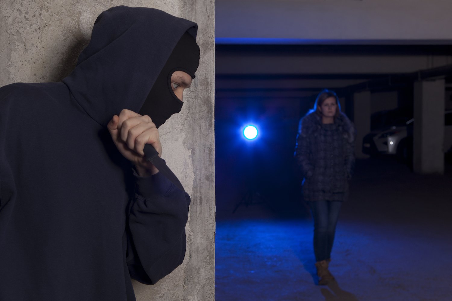 Hombre enmascarado con un cuchillo esperando detrás de una pared para matar a una víctima que camina por un callejón sin darse cuenta